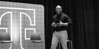 Speaker presenting onstage in front of a large “T” backdrop.