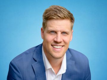Smiling man in a blue suit against a blue background.
