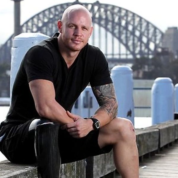 Man sitting on a waterfront ledge with a bridge in the background.