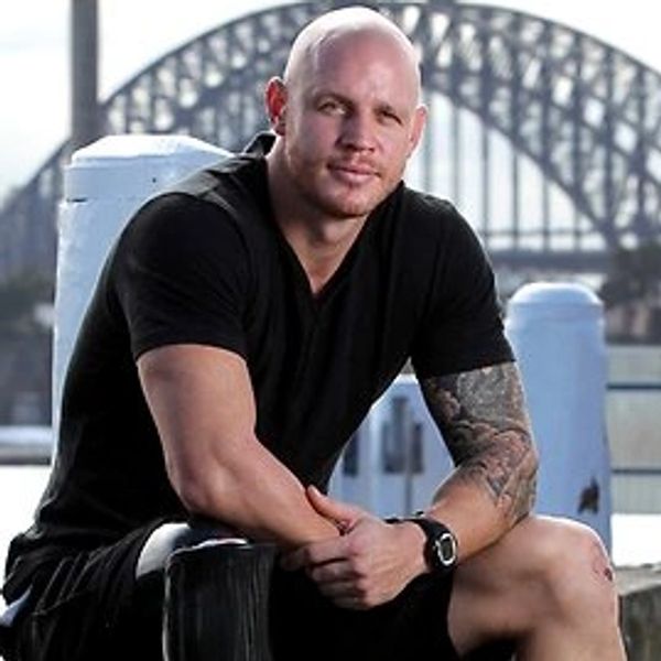 Man sitting on a waterfront ledge with a bridge in the background.