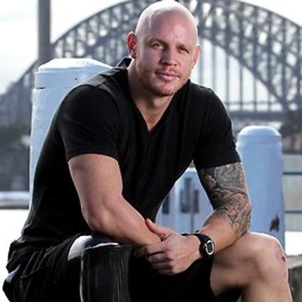 Man sitting on a waterfront ledge with a bridge in the background.