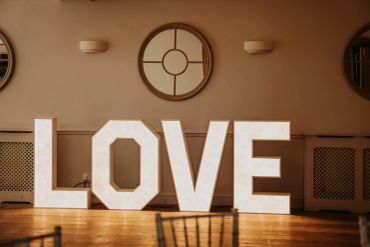 Illuminated LOVE sign inside a room with wooden floor.