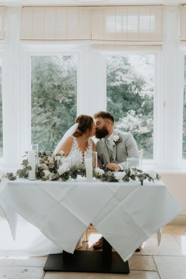 Bride and groom sharing a kiss at their wedding table.