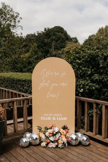 Wedding welcome sign with flowers and disco balls.