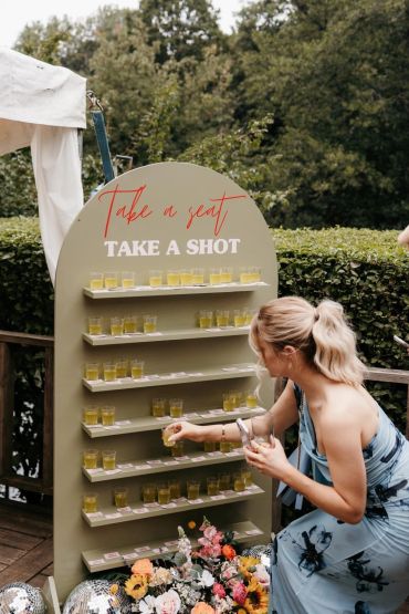 Woman picking a shot glass from a display board at an outdoor event.
