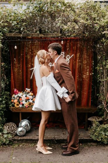 Bride and groom kissing outdoors under a wooden arch.