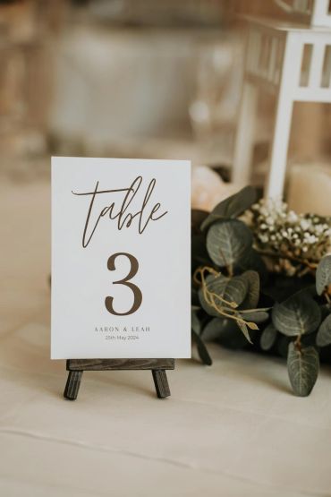 Elegant table number card with greenery on a wedding table.