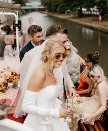 Bride smiling and holding a glass on a boat with guests.