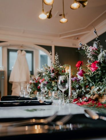 Wedding table setup with floral decorations and dress in background.