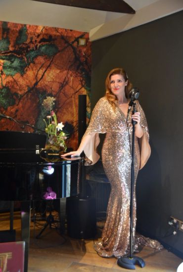 Woman in sparkling gold dress with vintage microphone near piano.