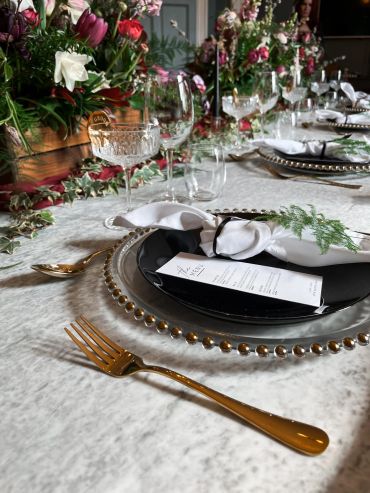 Elegant table setting with black plates and gold cutlery.