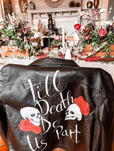 Leather jacket with skulls and roses design on a flower-decorated table.