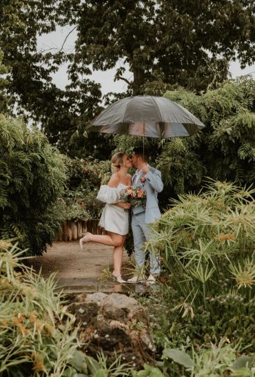 Couple kissing under an umbrella in a lush garden.