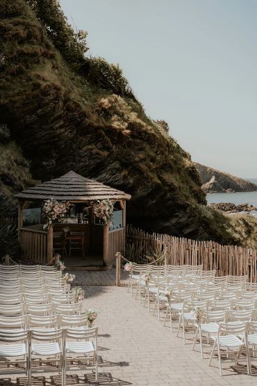 Outdoor wedding setup with floral-decorated gazebo by the sea.