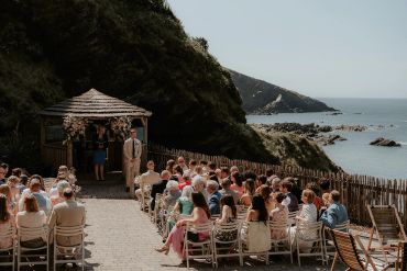 Outdoor wedding ceremony by the sea with guests seated.