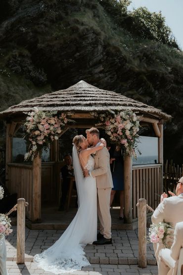 Bride and groom kissing under a flower-adorned gazebo.