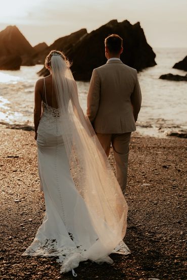 Bride and groom walking on a beach at sunset.