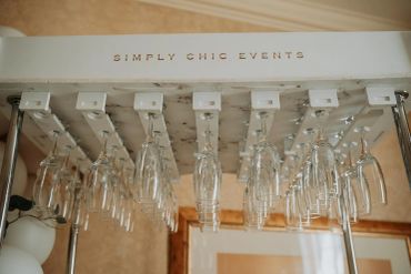 Upside-down wine glasses hanging on a rack labeled Simply Chic Events.