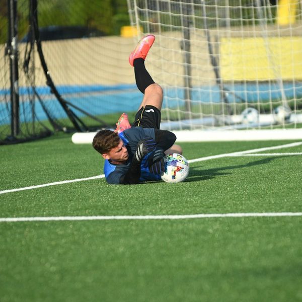 A soccer goalkeeper dives to catch the ball on the field.