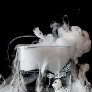 Glass with water and swirling white smoke on black background.