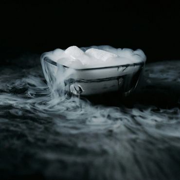 A glass bowl emits thick white smoke or vapor in a dark setting.