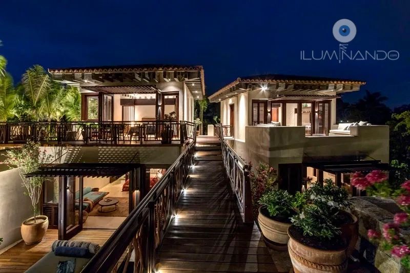 Pasarela iluminada conecta villas modernas con luz cálida, creando un ambiente acogedor y elegante.