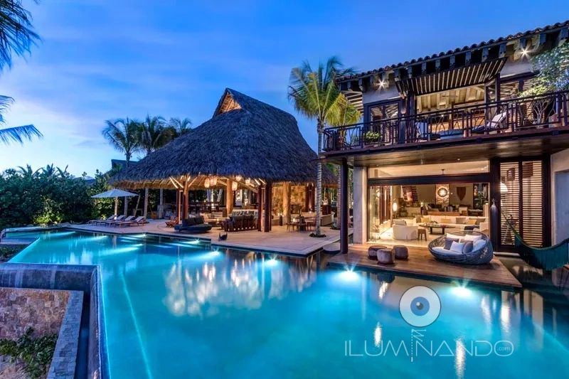 Iluminación destacada piscina, palapa y terraza, creando un ambiente tropical cálido y sofisticado