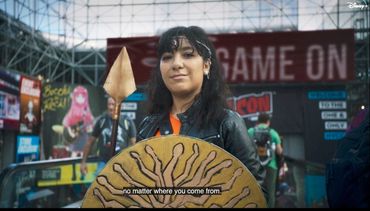 A person dressed as a warrior at a convention holding a spear and shield.