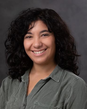 Smiling woman with curly hair wearing a green button-up shirt.