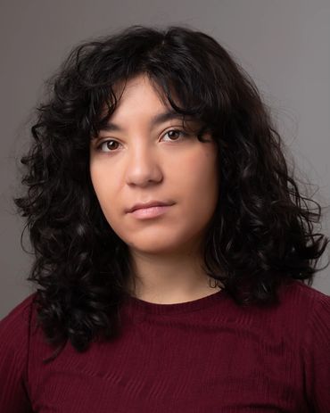 Portrait of a woman with curly dark hair wearing a maroon top against a gray background.