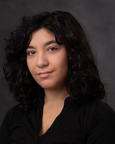 Portrait of a woman with curly hair and a subtle smile against a dark background.