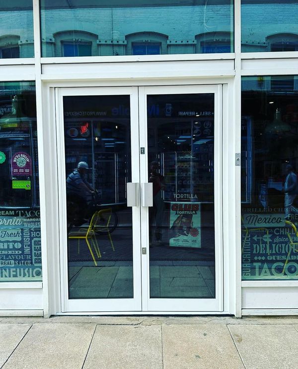 Reflective glass doors of a store showing street reflections and a cyclist passing by.