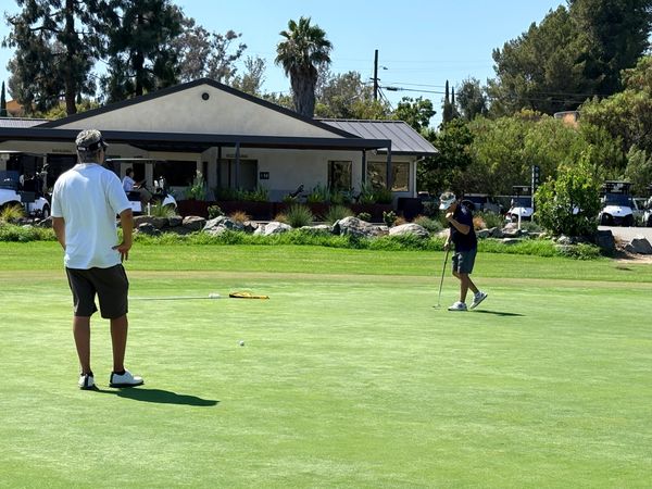 Two men playing golf on a sunny day near a building.