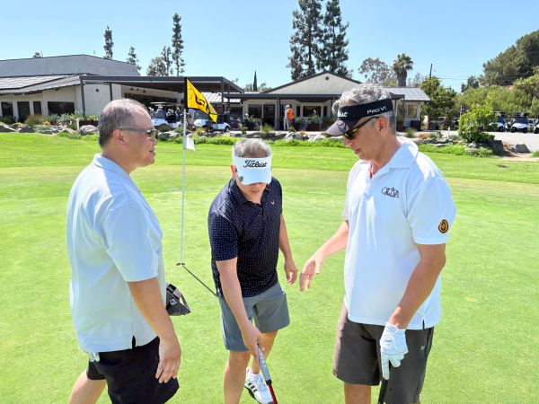 Three men standing on a golf course near the hole flag.