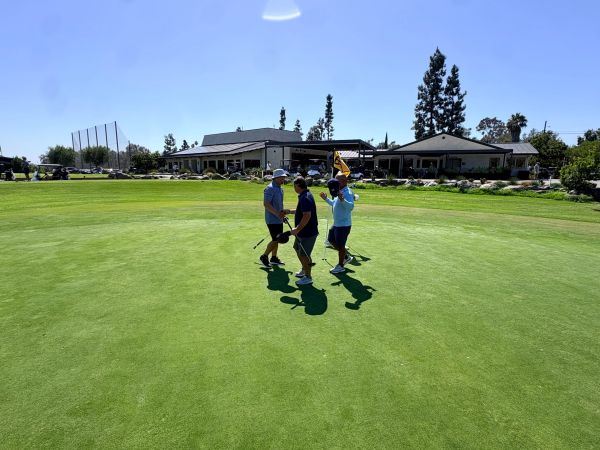 Four men celebrating on a golf course green under a clear sky.