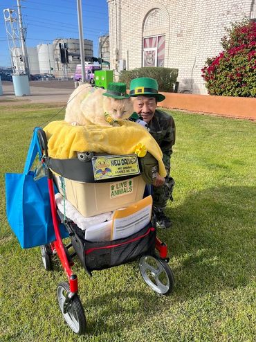 A cat and man wearing green hats with a walker and a container labeled live animals.