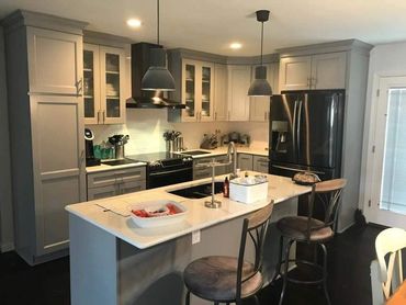 Modern kitchen with gray cabinets, black appliances, and a marble island with seating.