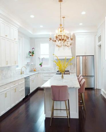Bright white kitchen with marble countertops and pink velvet stools under a crystal chandelier.