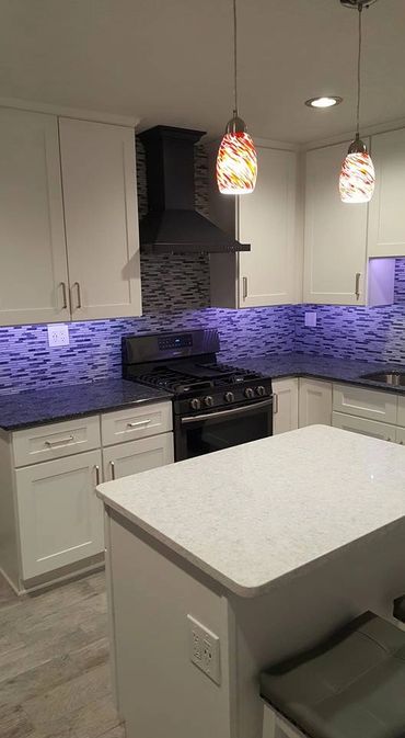 Modern kitchen with white cabinets, black stove, and blue LED backsplash lighting.