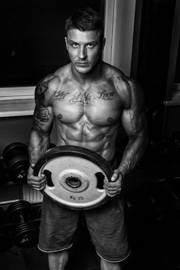 Muscular man holding a 20kg weight plate in a gym.