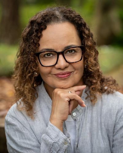 Thoughtful woman with curly hair and glasses outdoors.