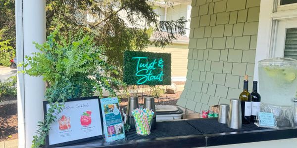 Outdoor bar setup with cocktail menu and neon Twist & Stout sign.