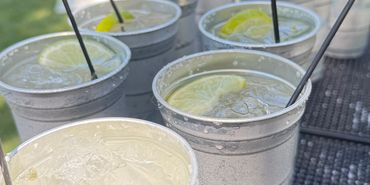 Chilled lemon drinks in gray aluminum cups with black straws on a sunny day.