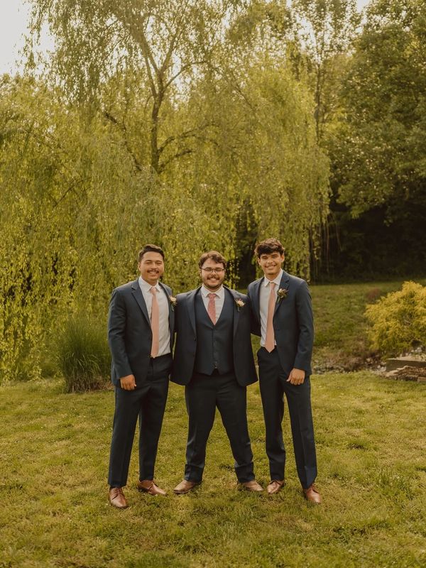 Three men in suits posing outdoors on grass.