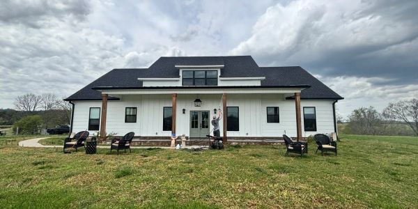 Modern farmhouse with seating on the porch and cloudy sky.