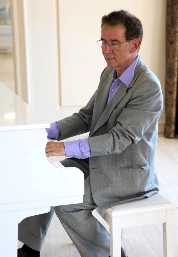 Man in a gray suit playing a white piano indoors.