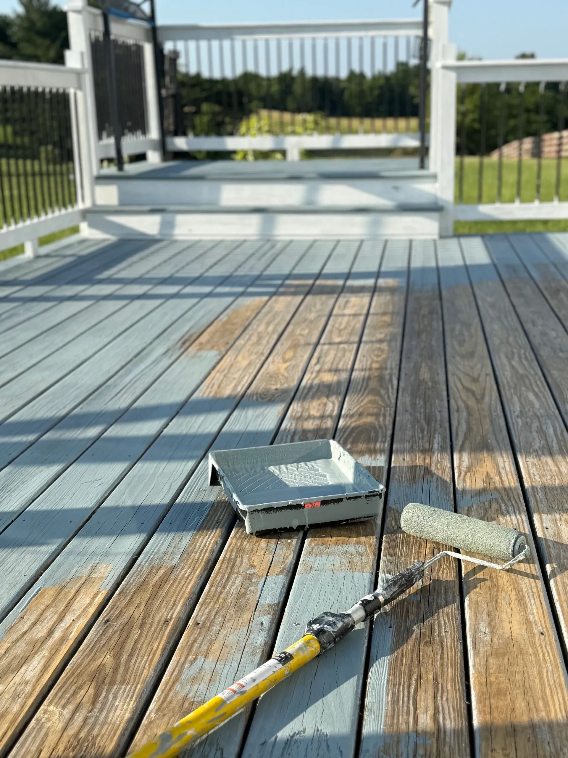 Deck being painted blue with a roller and tray on wooden planks.