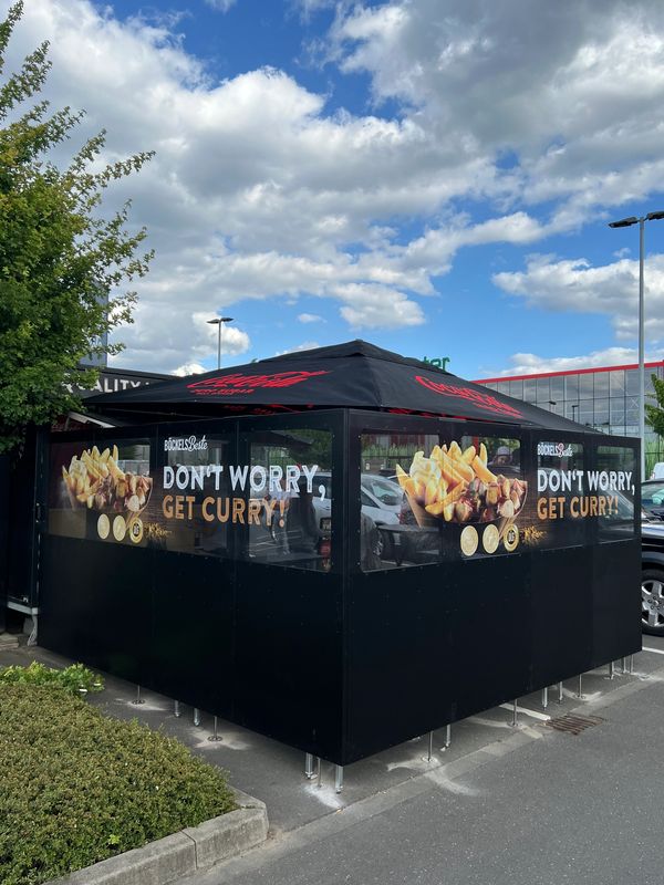 Outdoor food stall with signage saying 'Don't worry, get curry!' and images of currywurst and fries.