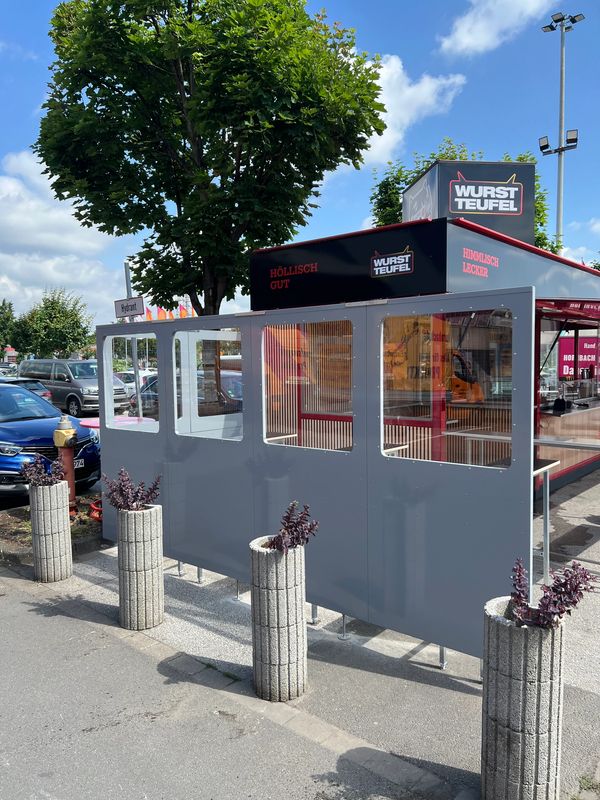 Outdoor seating area with protective panels at Wurst Teufel food stand.