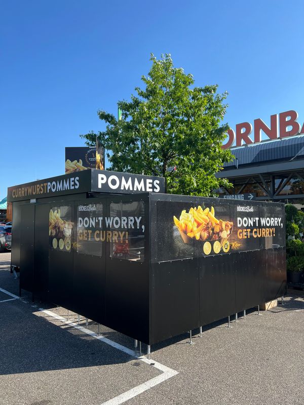 Outdoor food stall advertising currywurst and fries with the slogan 'Don't worry, get curry!'